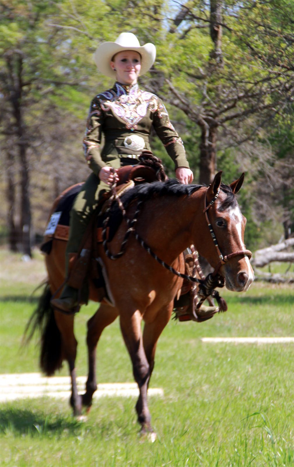 A rider in show attire sits on a bay horse in a green field at a show in Texas.